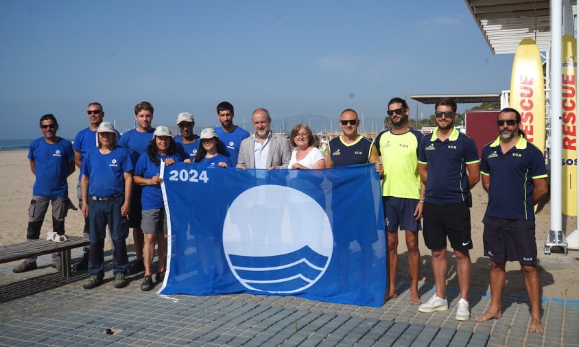 Autoritats i equip de socorristes posen amb la bandera blava a la platga del Cavet