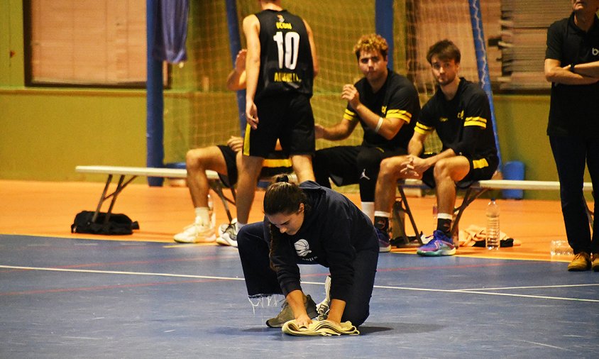 Una membre del CB Cambrils eixuga l'aigua de la pista mentre es disputa el partit de l'equip sènior entre el CB Cambrils i el CB Altafulla