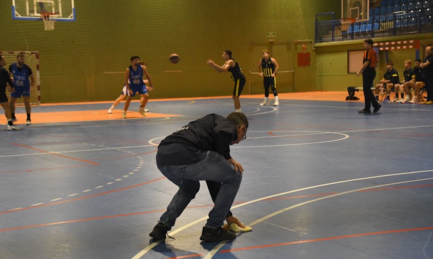 Un membre del Club Bàsquet Cambrils netejant, en ple partit, l'aigua caiguda a la pista per les goteres