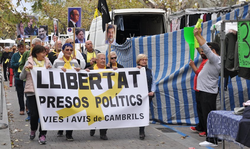 La manifestació dels Avis i Àvies al pas pel costat del mercadet on es veuen els dos venedors amb els cartells