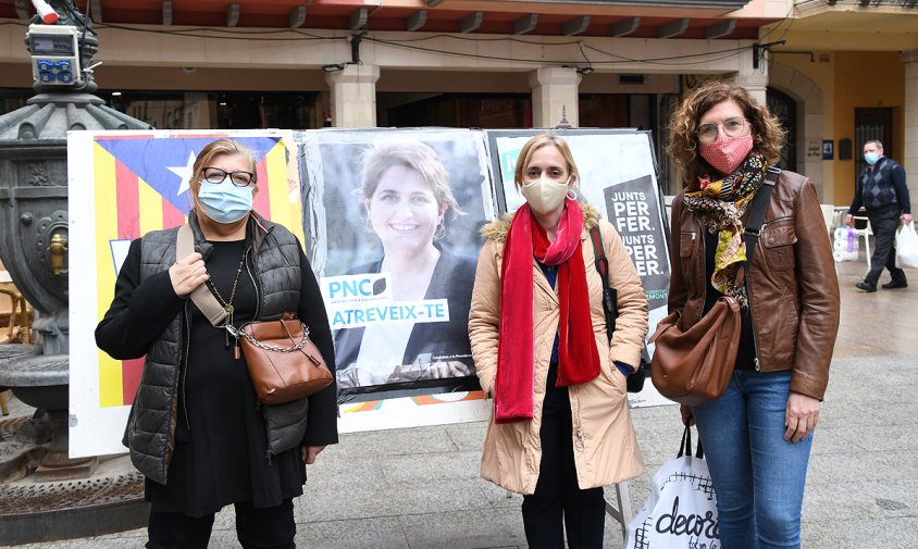 Margarida Colet, àurea Rodríguez i Mercè Dalmau, al costat d'un dels cartells de la seva formació, aquest migdia a la plaça de la Vila